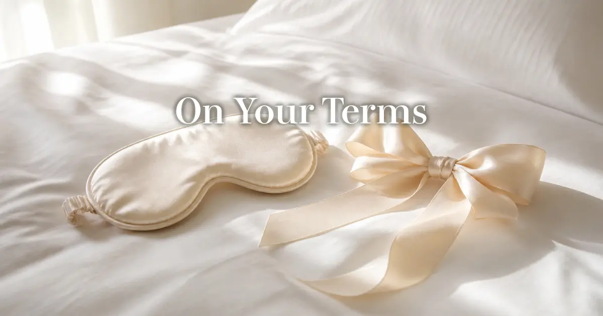 Silk blindfold and soft ribbon arranged on white hotel bedding in gentle light